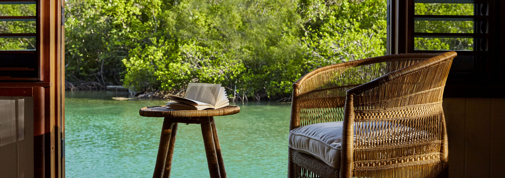 Aufgeschlagenes Buch auf einer Sitzgruppe einer Terrasse direkt am Meer mit tropischem Hintergrund