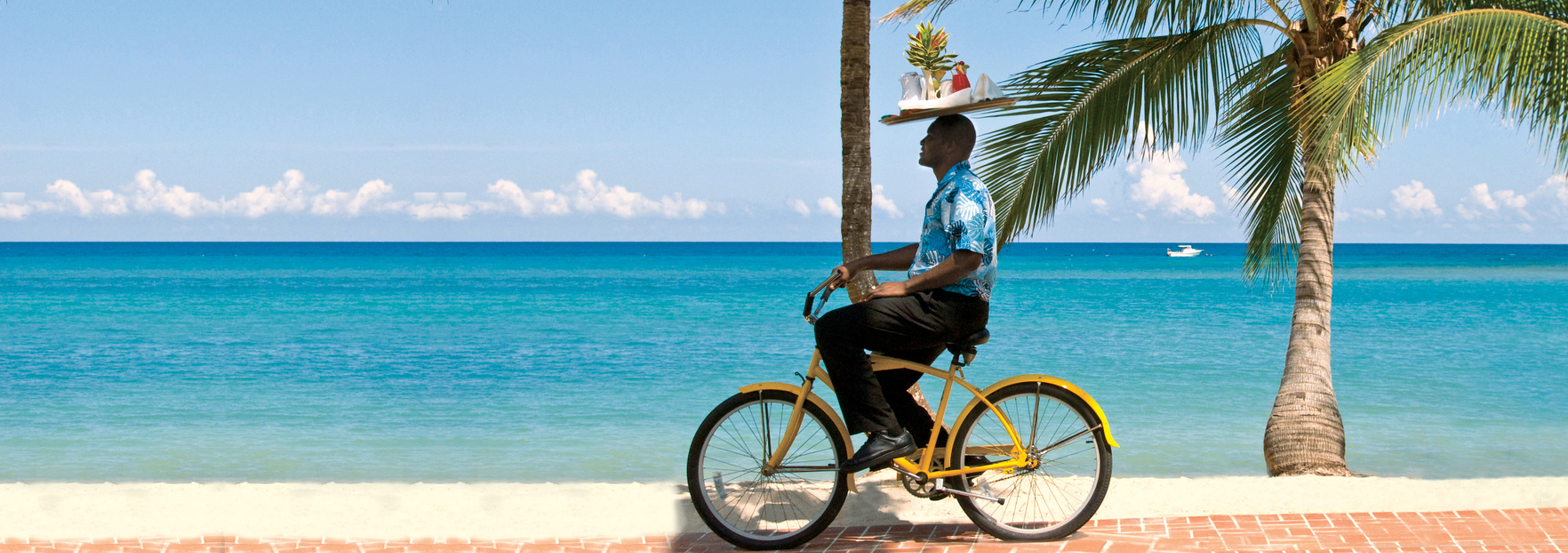 Radfahrer am Strand mit Tablett auf dem Kopf im Half Moon Resort auf Jamaica