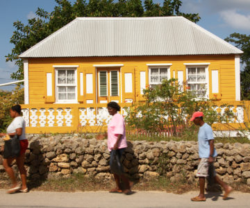Drei Fußgänger vor einem weiß-gelben Holzhaus auf Anguilla