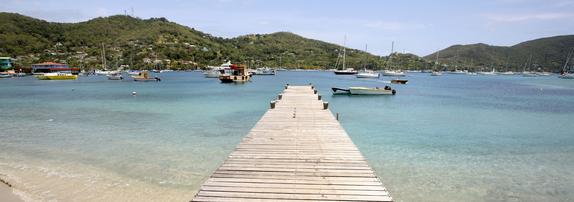 Steg in einer Bucht auf Bequia mit ankernden Jachten und Fischerbooten